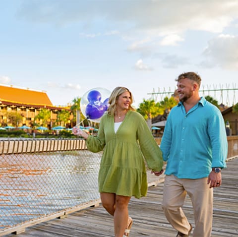 A man and a woman with a Mickey Mouse balloon holding hands and smiling while taking a walk at Disney's Polynesian Villas and Bungalows A man and a woman with a Mickey Mouse balloon holding hands and smiling while taking a walk at Disney's Polynesian Villas and Bungalows