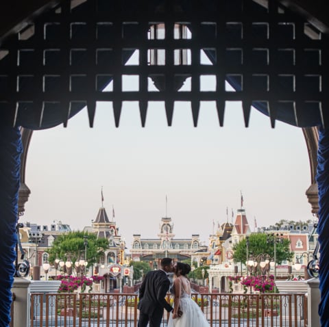 A bride and groom pose beneath a wrought iron gate at Cinderella Castle at Walt Disney World Resort