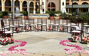 Rose petals lead to a group of chairs arranged in a semi circle on a courtyard with a large water fountain