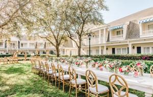 A garden venue decorated for a wedding reception with a long table, chairs and flowers in vases at Poolside Green at Disney’s BoardWalk Inn A garden venue decorated for a wedding reception with a long table, chairs and flowers in vases at Poolside Green at Disney’s BoardWalk Inn