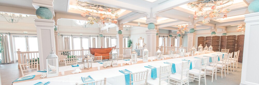 Several chairs around a long table decorated with seashells and lanterns under ornate hanging decorations