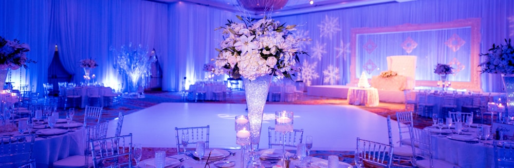Large snowflakes are projected on the walls and tall floral arrangements rest on tables in the middle of a ballroom