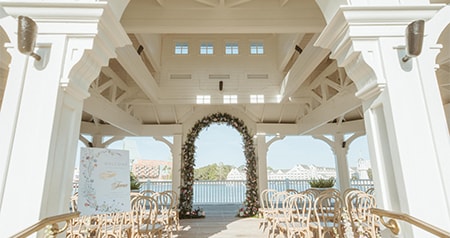 An outside gazebo ceremony setup with wooden chairs, a floral arch and a scenic waterfront backdrop