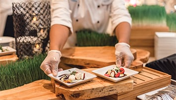 A chef places 2 small square plates on a wooden table