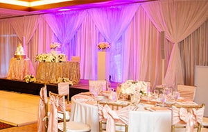 A dance floor in the middle of a reception hall holding several round tables and a cake table