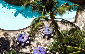 Several round tables arranged on a patio near a long pool