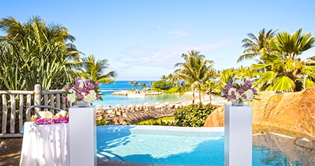 Two vases of flowers on pillars near a pool overlooking a beach