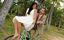 A bride sits on the handlebars while the groom pedals a bike