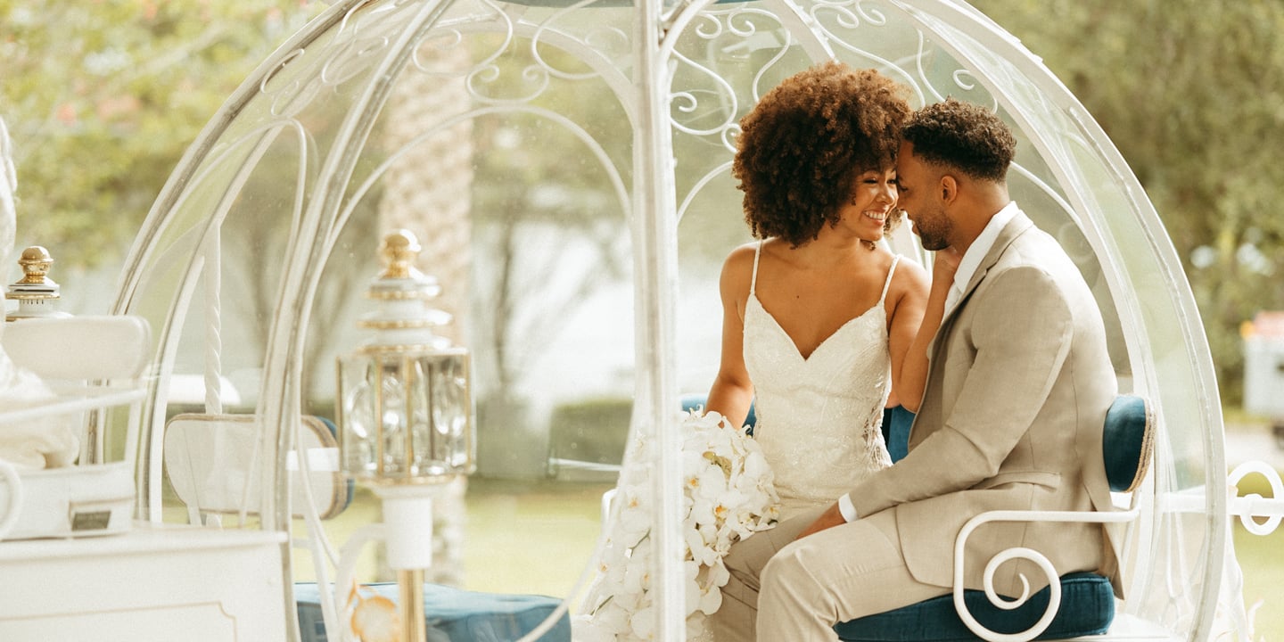 A smiling bride and groom sitting on a sofa and holding Mickey Mouse ice cream bars