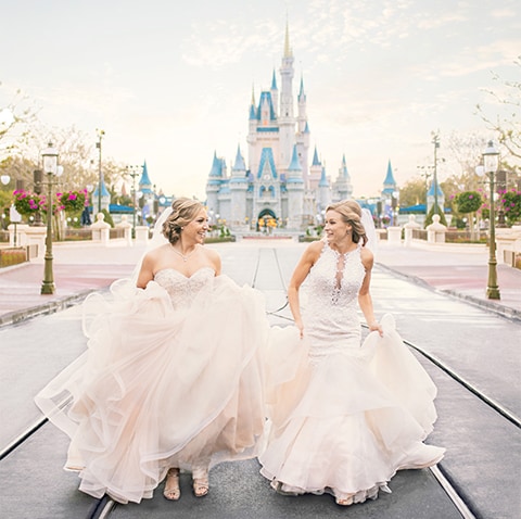 Two females in wedding dress in front of Cinderella's Castle