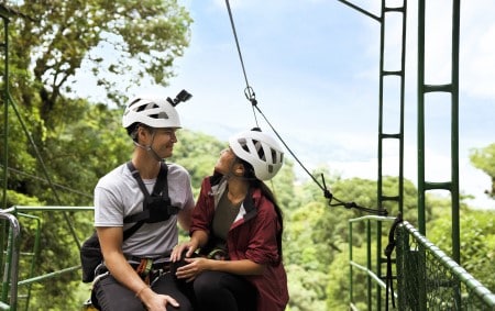 Smiling newlyweds with ziplining equipment in the treetops of a jungle in Costa Rica