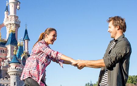 A man pulls a laughing woman towards him by Sleeping Beauty Castle 