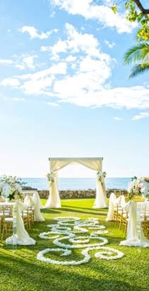On a lawn overlooking the water, chairs arranged for an outdoor wedding face an alter draped with fabric On a lawn overlooking the water, chairs arranged for an outdoor wedding face an alter draped with fabric