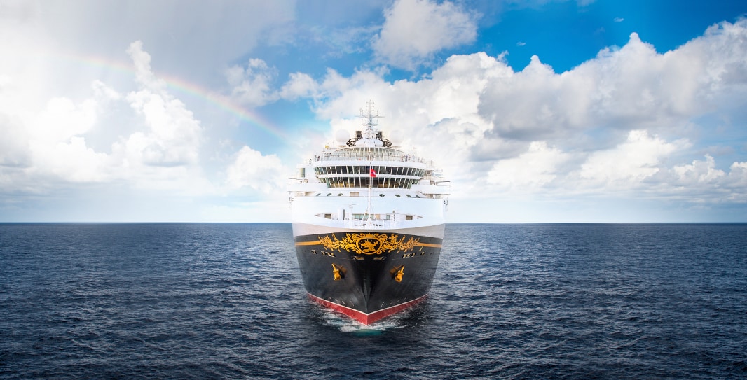a disney cruise line ship sails on calm seas with a partly