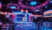 A supper club setting with a stage, a large movie screen and special effects lighting