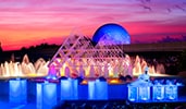 A chef sets up buffet and drink stations in front of a fountain with a pyramid sculpture design

