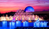 A smiling chef standing behind an illuminated food station at sunset near an active fountain with Spaceship Earth at Epcot in the distance