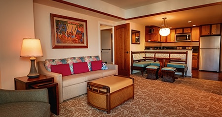 A hotel suite with a sofa, chair, ottoman, breakfast nook and kitchen
