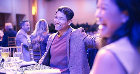 Guests seated at a dining hall and a man smiling
