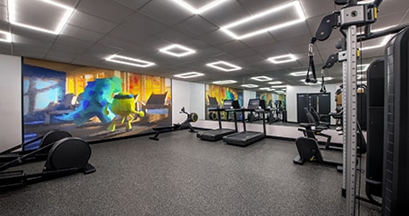 A hotel fitness center with exercise equipment, mirrors and a Monsters Inc mural featuring Mike and Sulley
