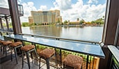 A counter with a row of stools at Villa del Lago lounge overlooks the water with Gran Destino Tower at Disney Coronado Springs Resort in the distance