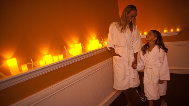 A mother and daughter wearing robes in a hall filled with lit candles on shelves