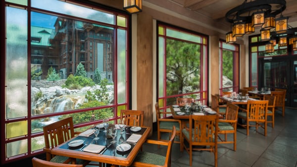 Set dinner tables in a rustic restaurant overlooking a waterfall and Disney's Wilderness Lodge