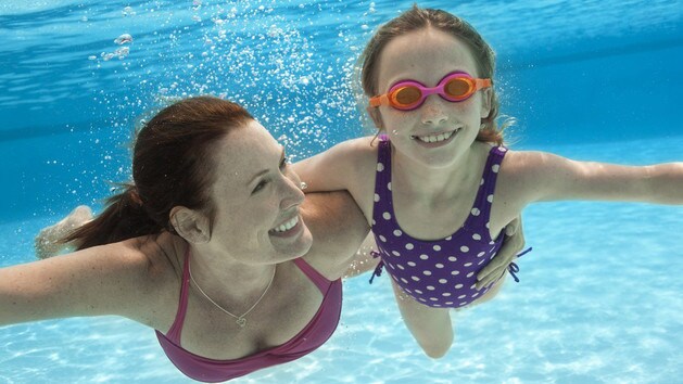 水中を泳ぎながら腕を組む、ゴーグルを着けた女の子と母親