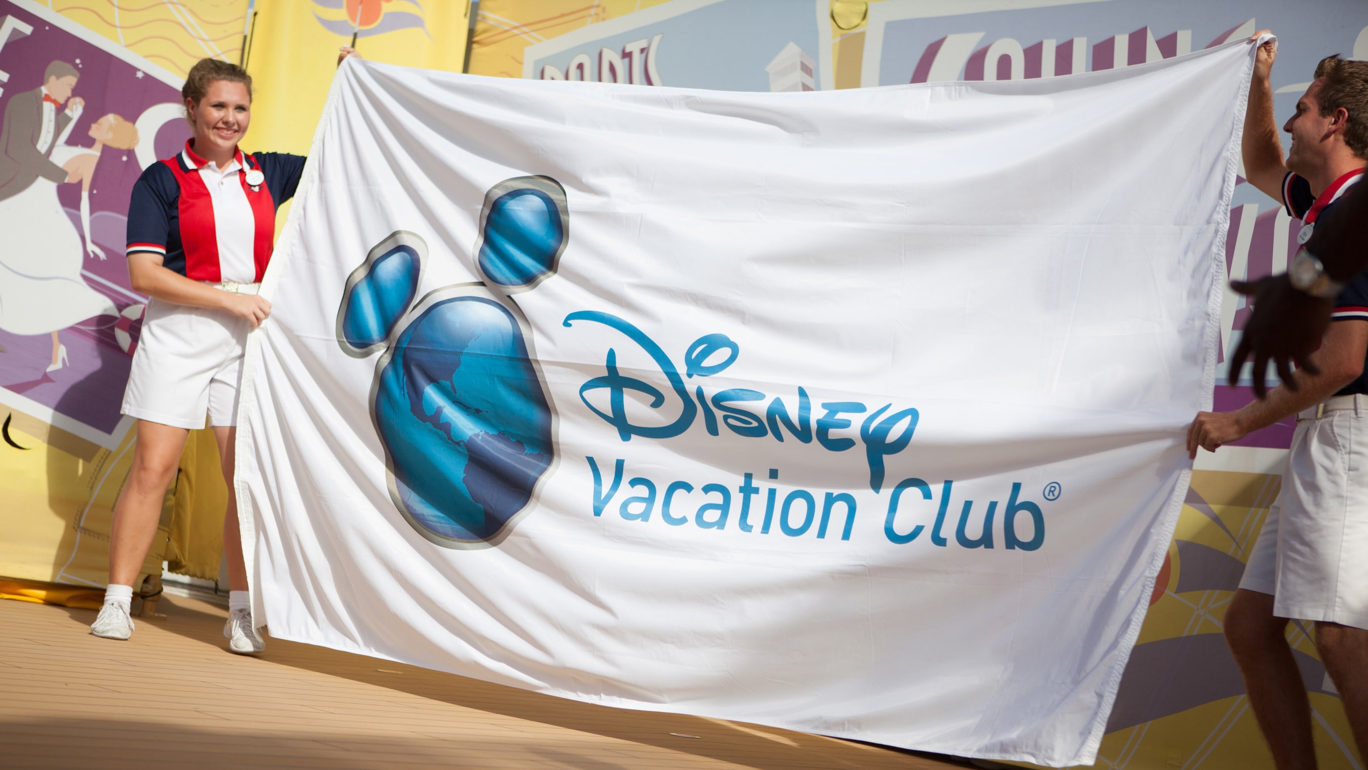 Two Disney Crew Members holding a large Disney Vacation Club flag