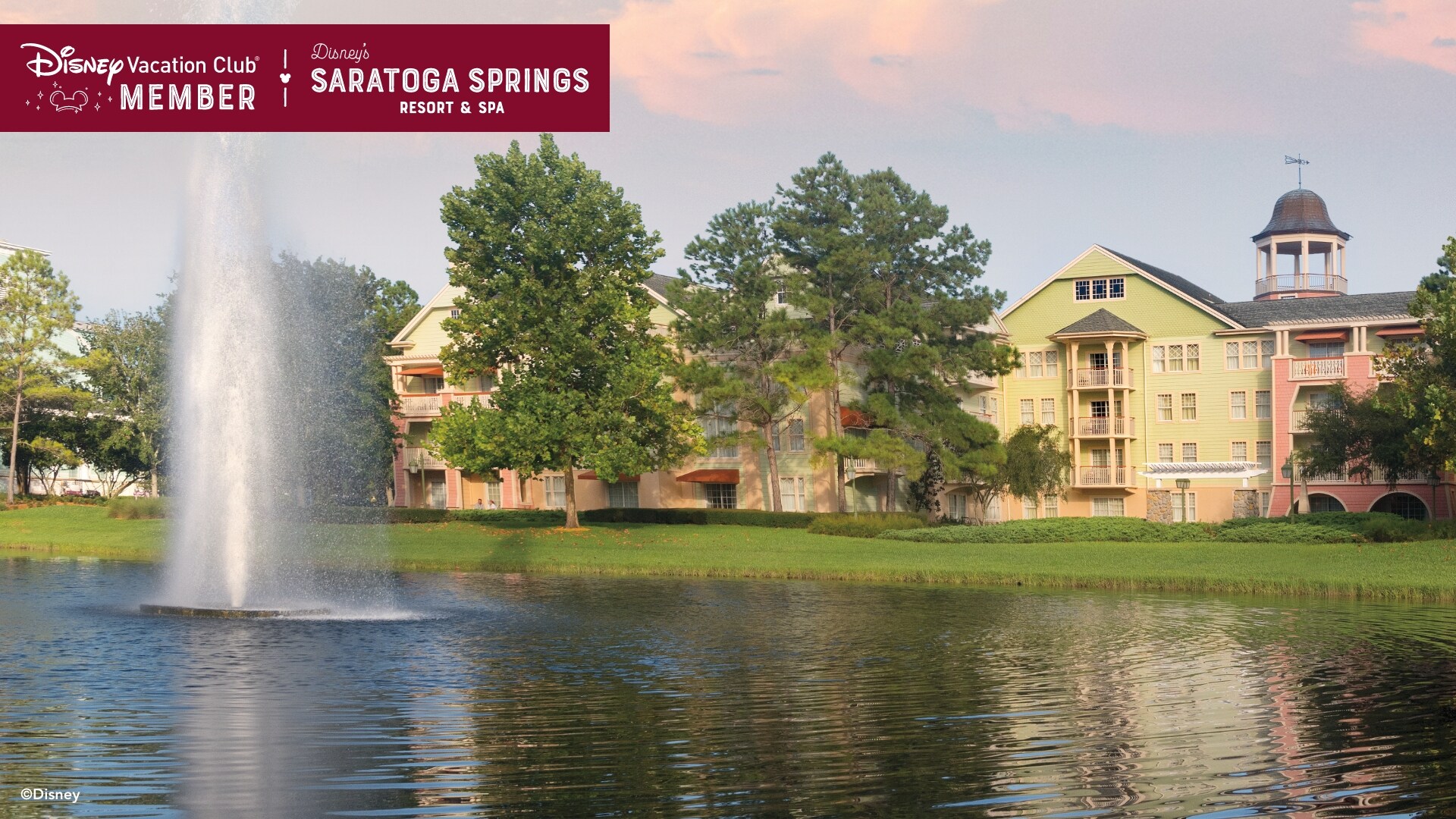 A fountain in the middle of a body of water sprays in front of Disney’s Saratoga Springs Resort and Spa, over which a banner reads, ‘Disney Vacation Club Member, Disney’s Saratoga Springs Resort and Spa’