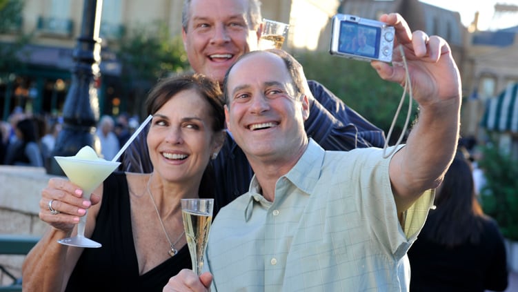 A woman with 2 men raising their beverages while taking a selfie