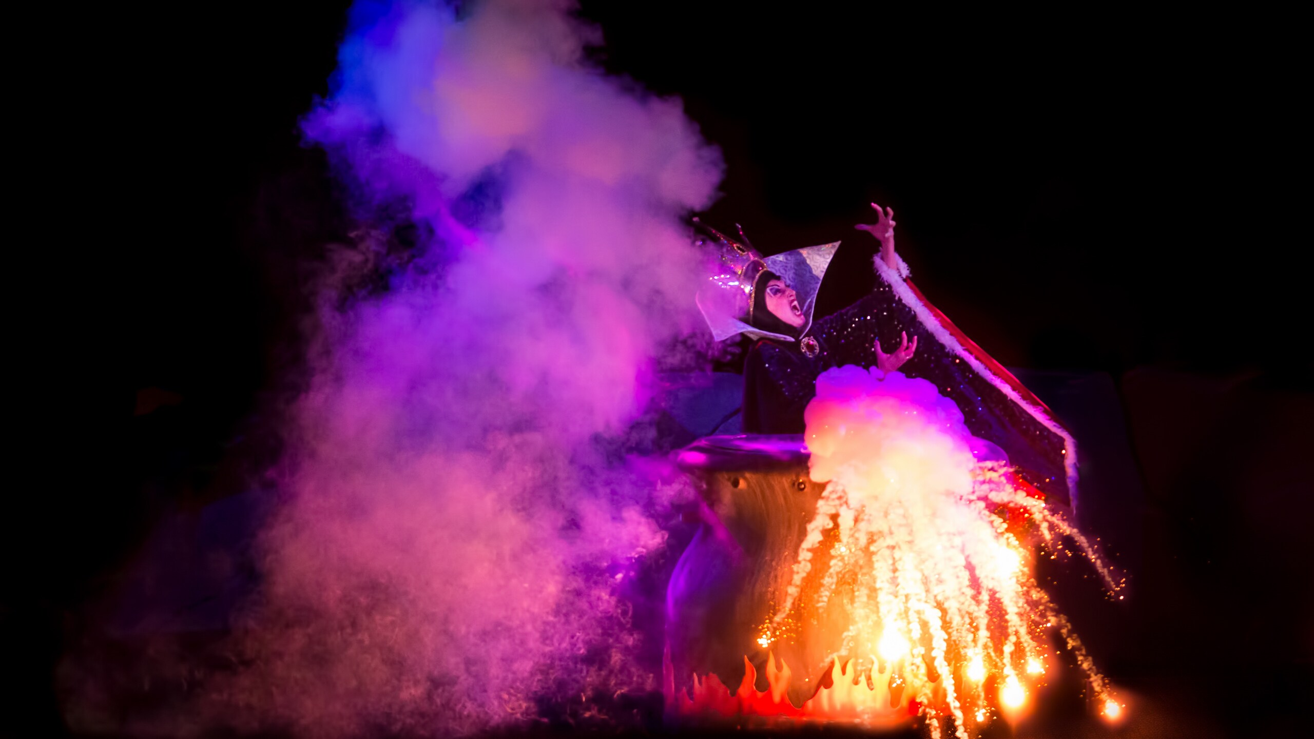 Maleficent stands beside a smoking cauldron
