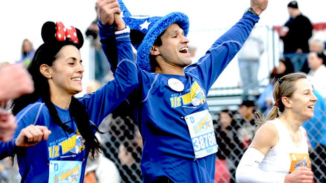 A man and woman running a race while wearing Mickey and Minnie Mouse ears