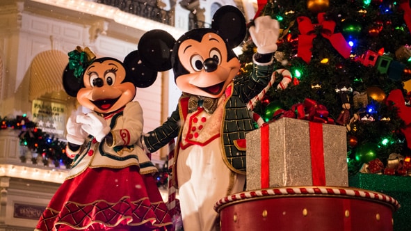 Mickey and Minnie Mouse dressed in holiday attire, standing beside a Christmas tree and presents