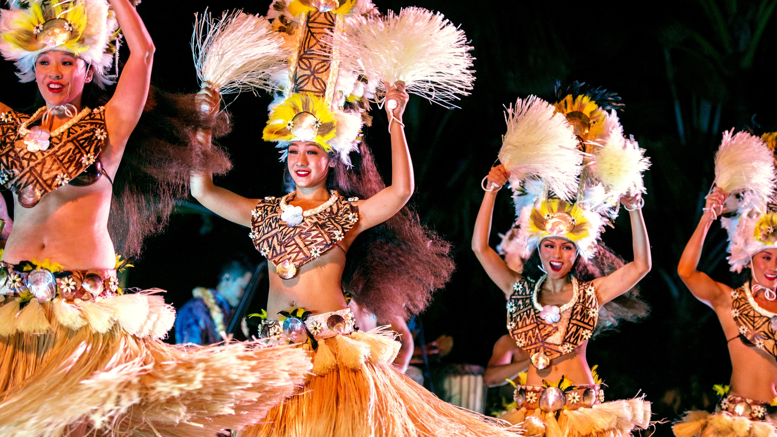 Several Hawaiian dancers wearing grass skirts and elaborate headdresses