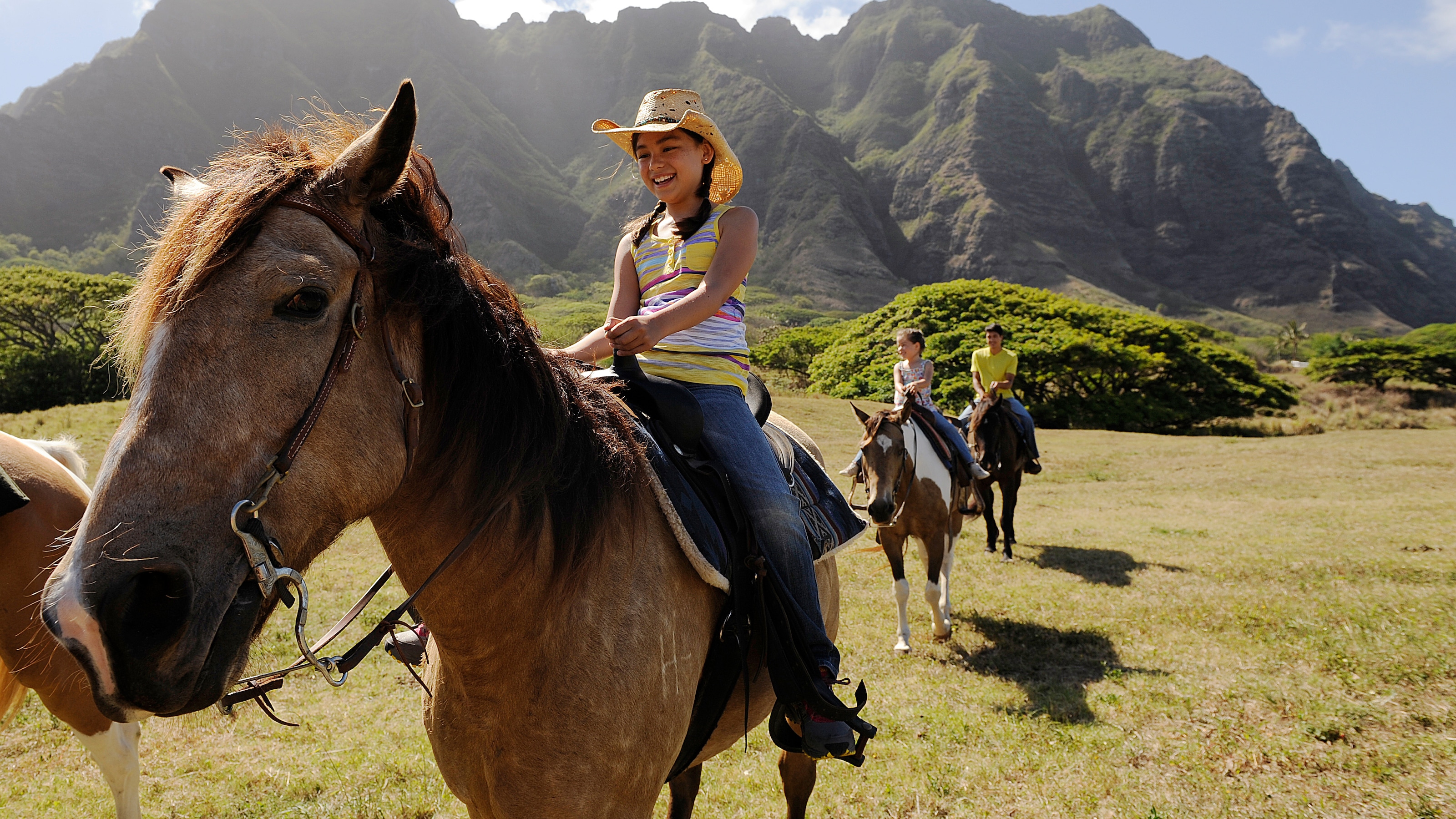 Several people riding horses in a lush valley in Hawaii