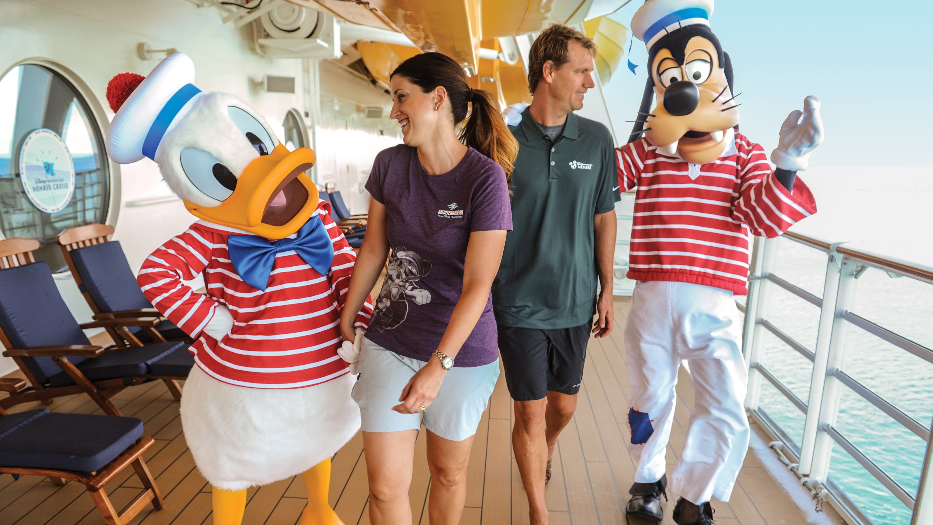 Donald Duck and Goofy walking with a man and a woman on the deck of a Disney cruise ship
