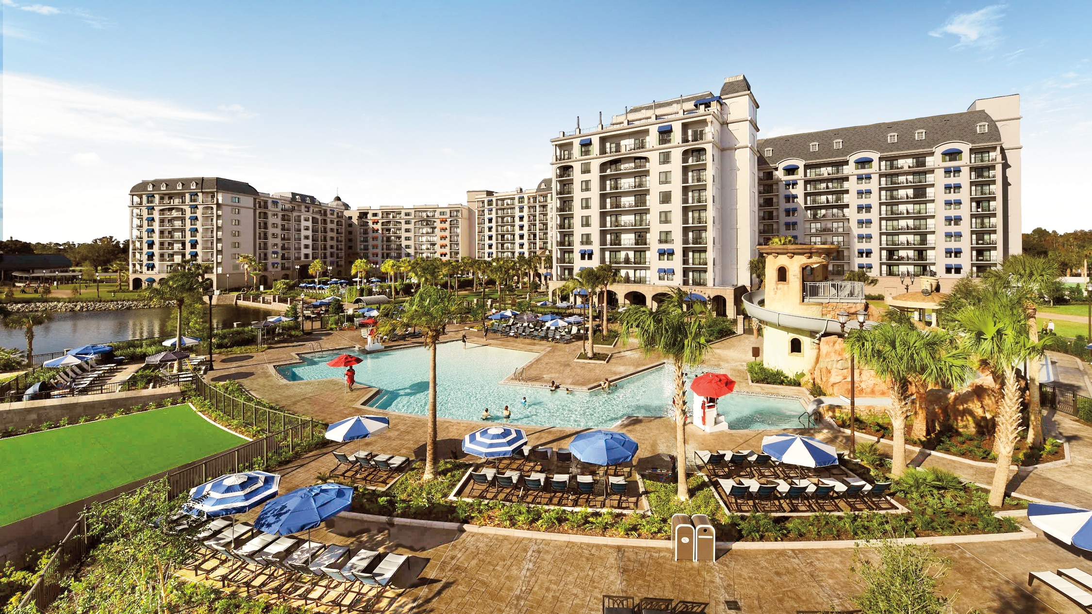 Disney’s Riviera Resort – On Sale Now An outdoor pool with a waterslide, surrounded by lounge chairs, umbrellas and palm trees at Disney's Riviera Resort
