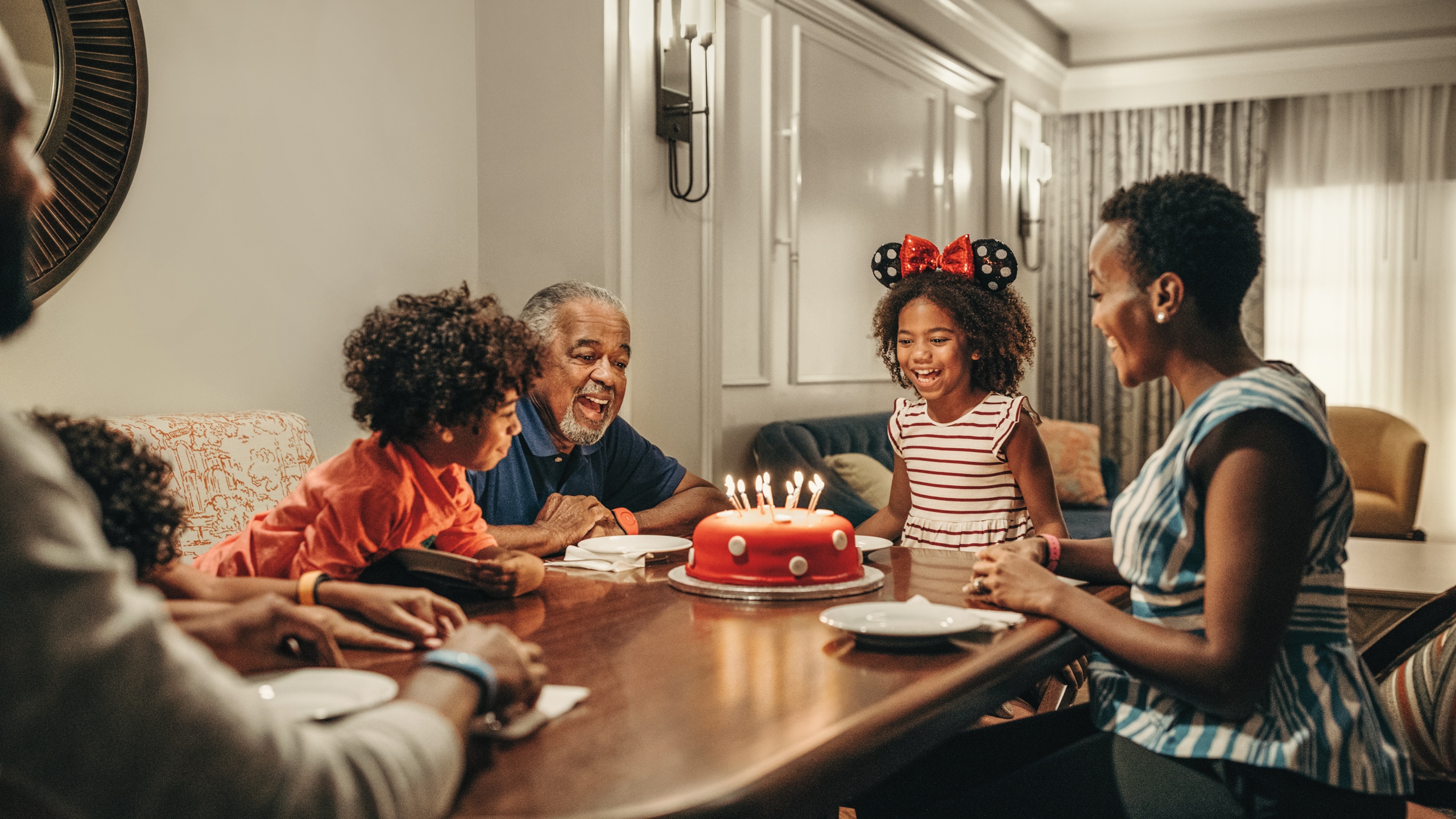 A family of 6 sits at a kitchen table at Disney’s Riviera Resort, ready to enjoy birthday cake