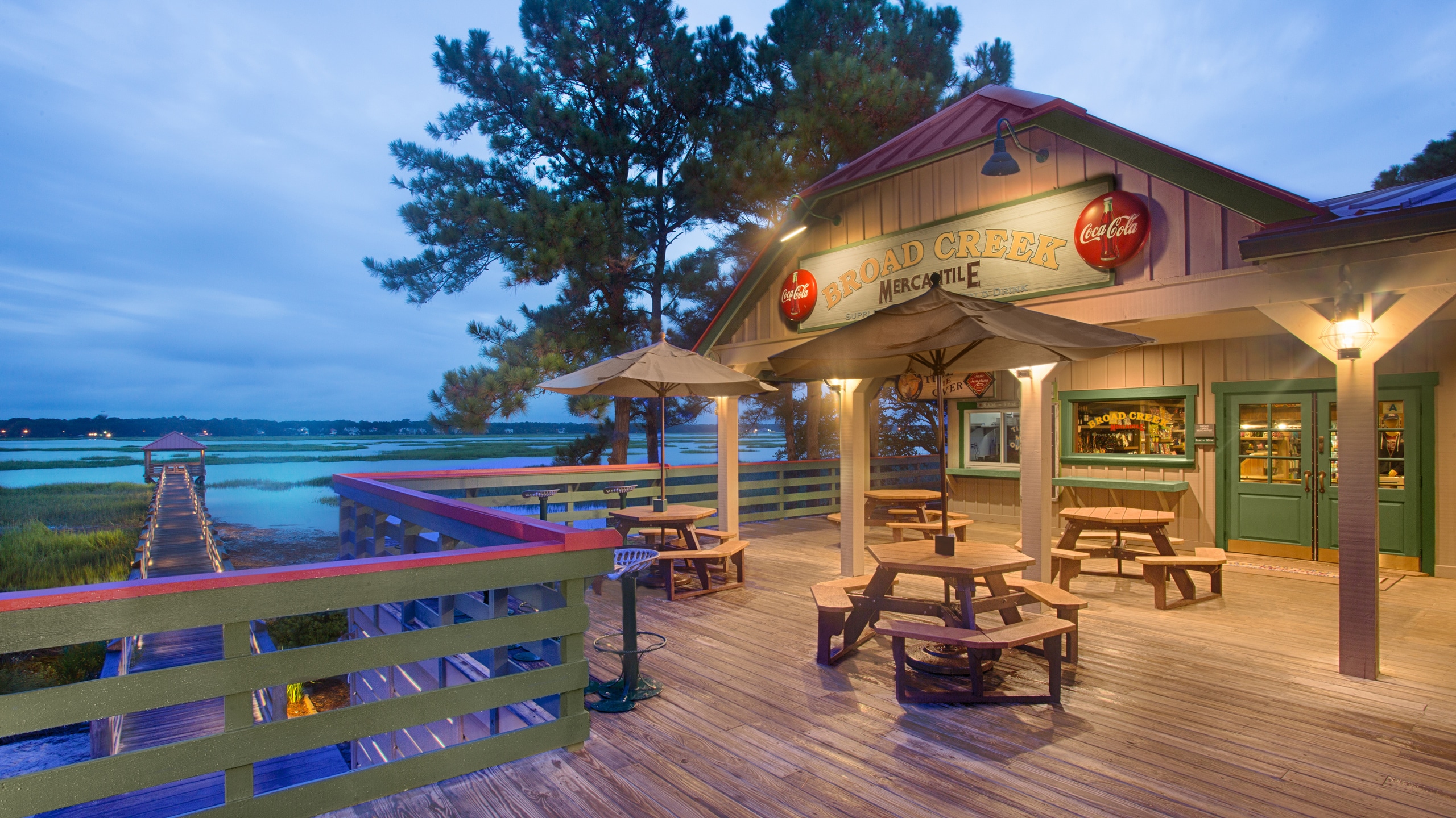 A boardwalk and pier under an elevated deck with seating and a storefront that says 'Broad Creek Mercantile'
