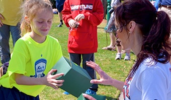 A woman delivers a box lunch to a girl on a sports field