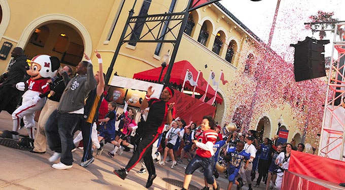 Home Slide - Parade Football Mickey and Guests march under the entrance sign to ESPN Wide World of Sports Complex
