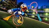 A statue of Donald Duck holding a tennis racket on the lawn of Disney’s All-Star Sports Resort with a 3 story high tennis racket and ball on the side of the hotel