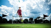 Challenge 3v3 National Championship A soccer player jumping for a ball while a goalie stands behind him