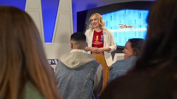A woman speaks to a room of people in front of a TV screen that reads ‘Disney Imagination Campus’