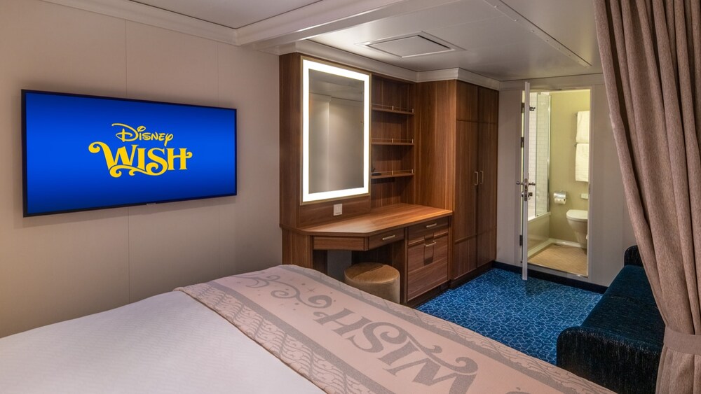 A Disney Wish Inside Stateroom with a bed, desk, mirror, TV, sofa and a bathroom