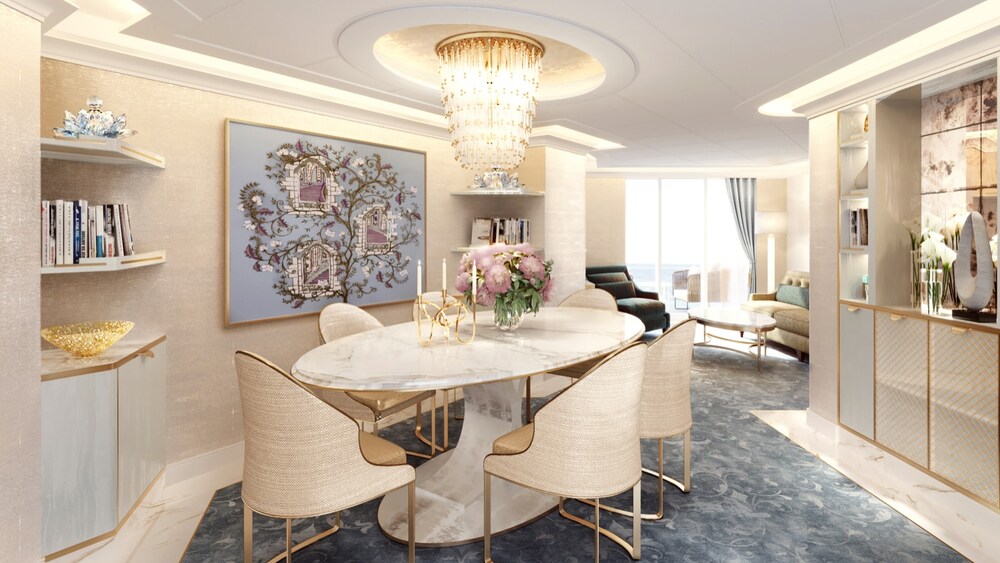 A Disney Wish Concierge One Story Royal Suite with Verandah living area with a sofa, chair, coffee table, chandelier, shelves, artwork inspired by Sleeping Beauty and a dining table with chairs 