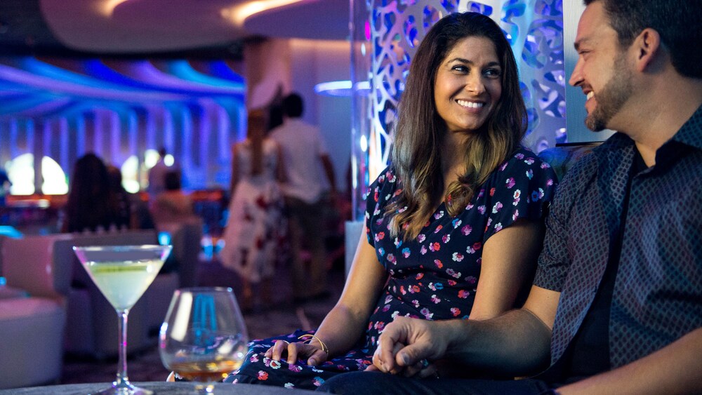 A man and woman smile at each other while enjoying cocktails in a club setting