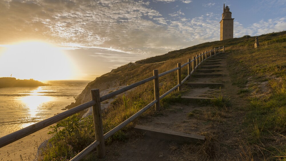 A stone lighthouse on a grassy hill next to the ocean