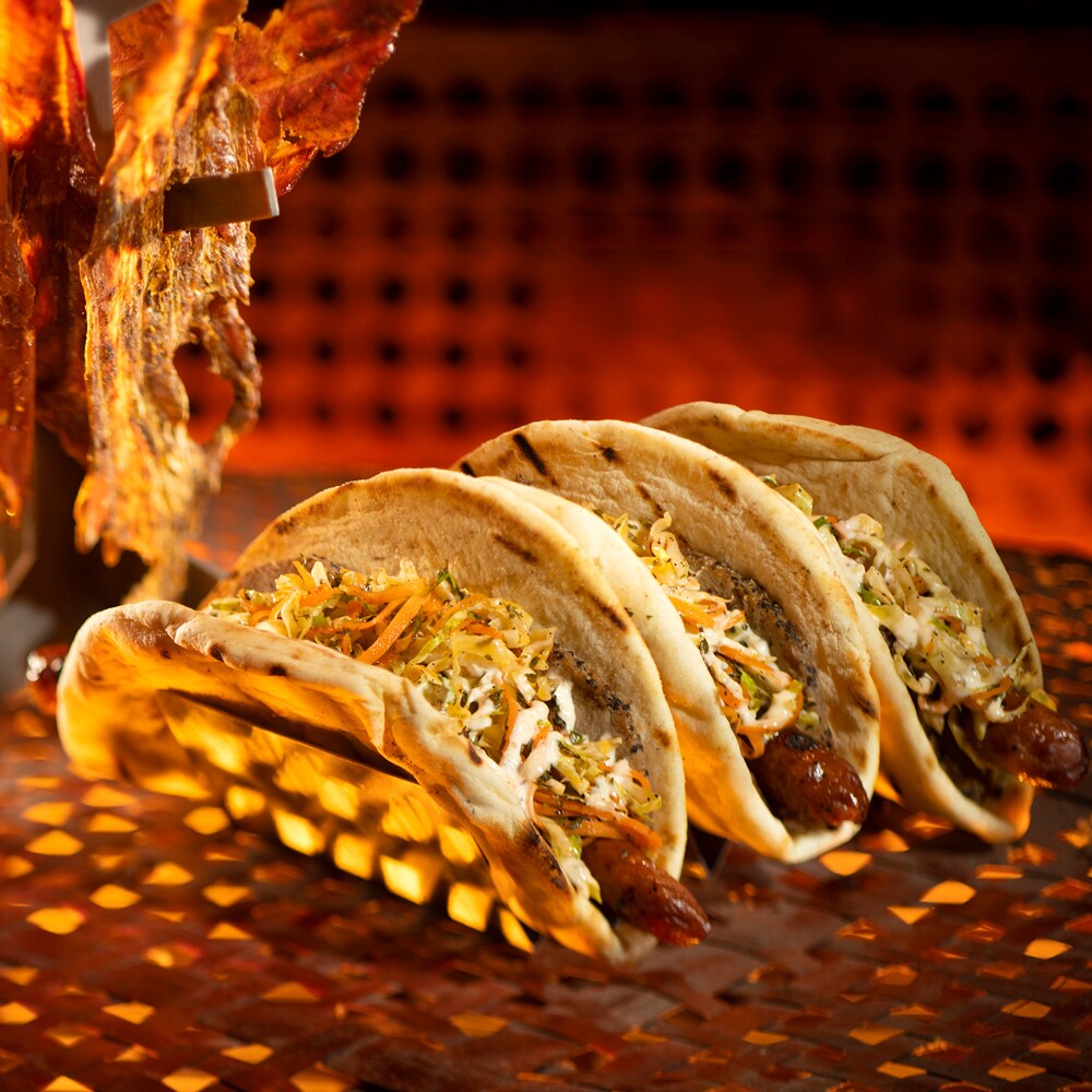 An exotic beverage and 3 thick tortillas filled with sausage, coleslaw and sauce